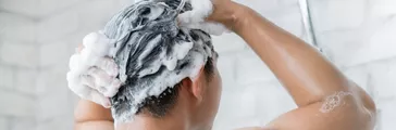 back view of man washing his air in a large tile shower