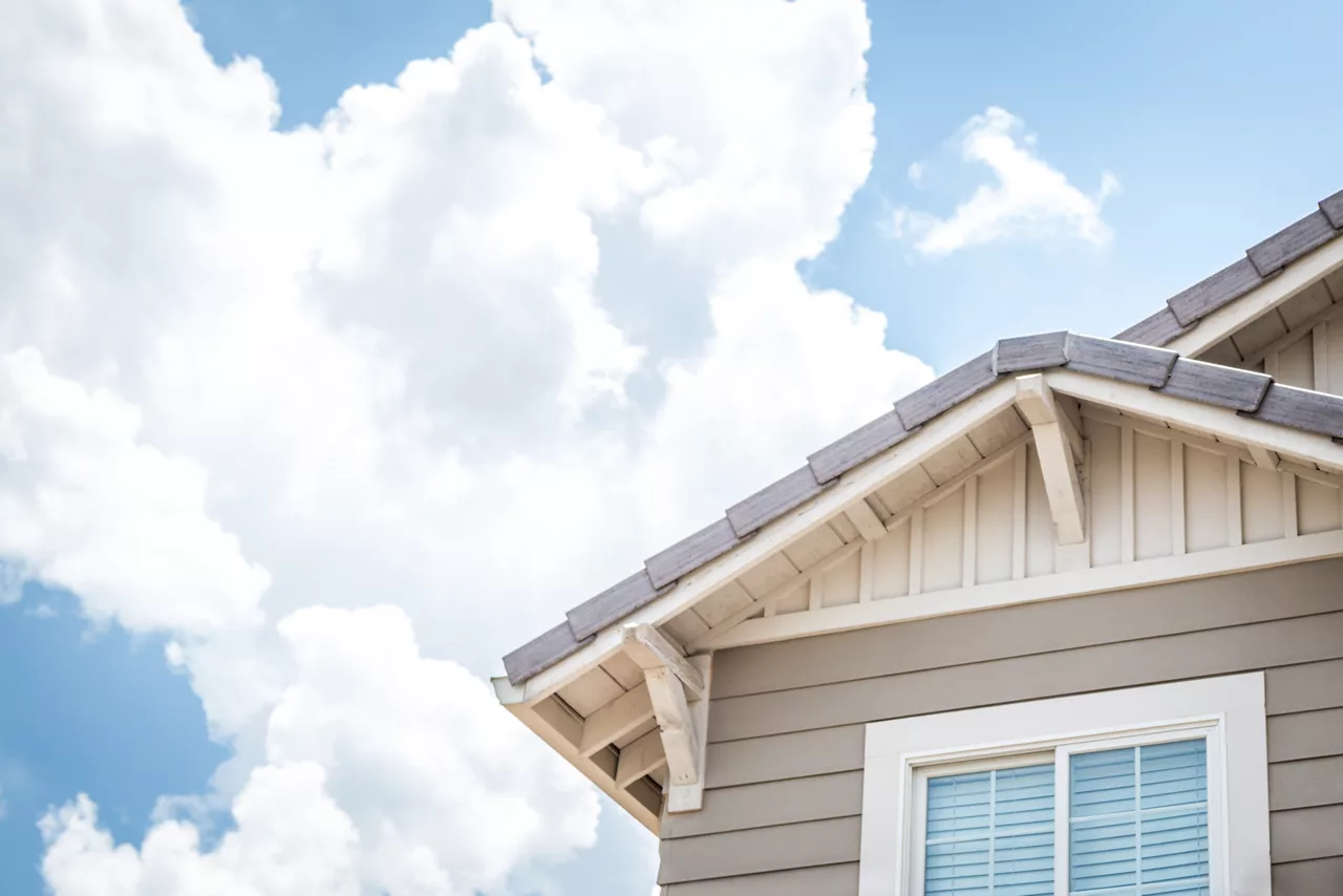 Coin de maison avec fenêtre et toit avec nuages blancs et ciel bleu en arrière-plan