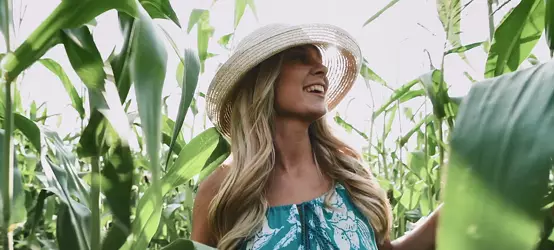 Giovane donna bionda con abito e cappello che cammina in un campo di grano.